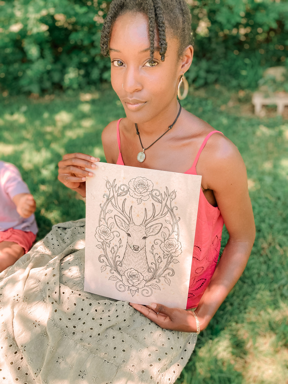 Black mother artist drawing beside her sleeping daughter in a woodland arch